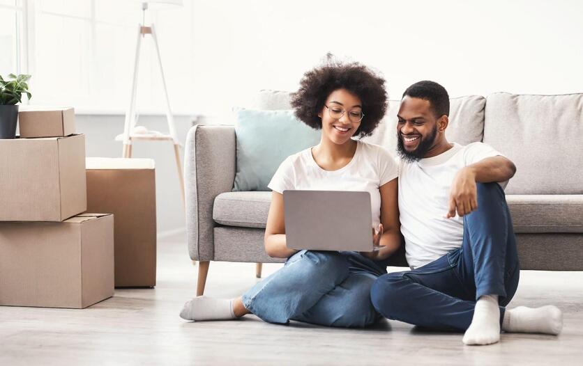 Duas pessoas sentadas no chão utilizando um computador. Ao lado, existem caixas de papelão.