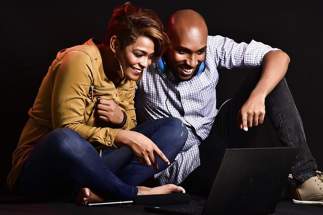 A imagem mostra um casal sentado no chão e interagindo com a tela de um computador para ilustrar o relacionamento com os pais por vídeo chamada após sair de casa