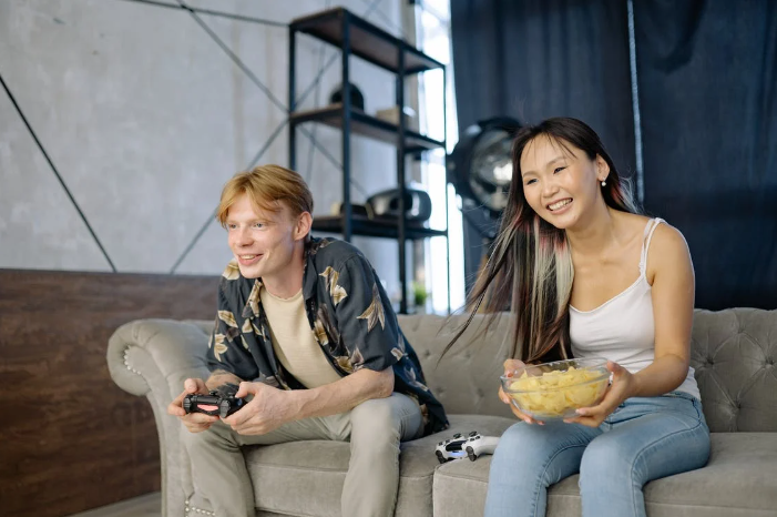 Um menino jogando vídeo game e uma menina comendo batatas no sofá da sala