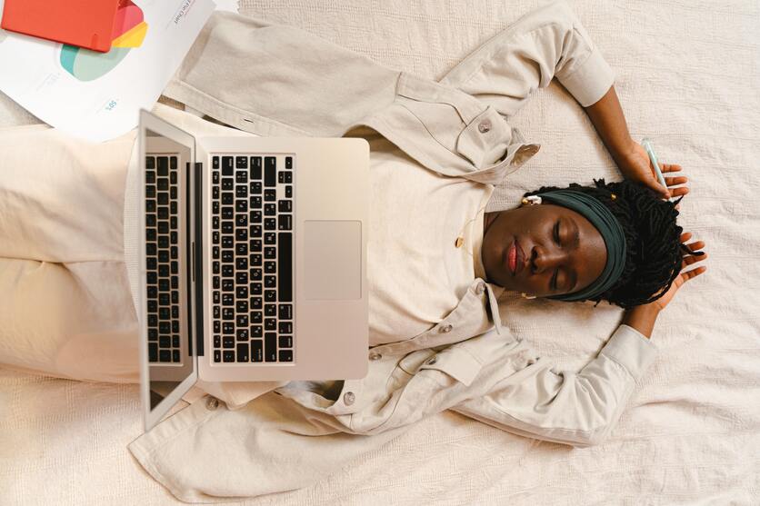 A imagem mostra uma mulher deitada, vista de cima, com o notebook aberto em cima da barriga para ilustrar as pausas dentro de uma rotina organizada