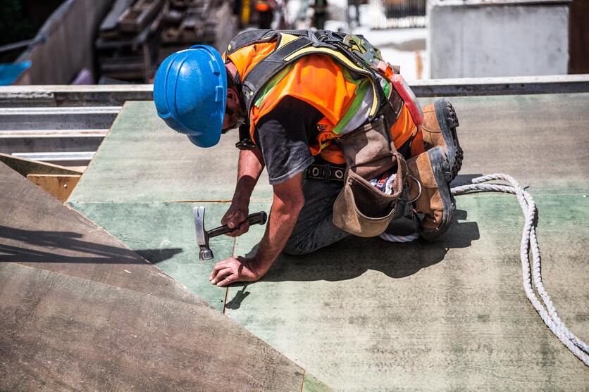 A imagem mostra um homem trabalhando em cima de um telhado com equipamento de segurança, para ilustrar o cuidado que uma empresa verde deve ter com a segurança de seus colaboradores