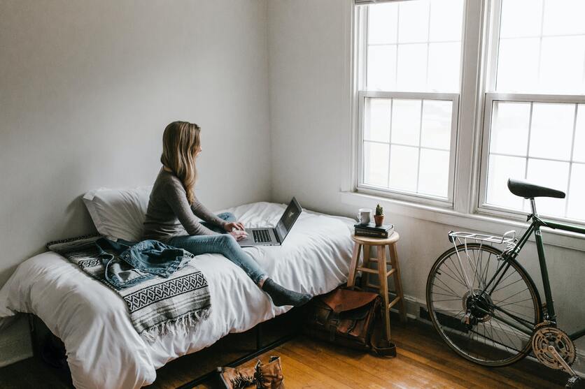 A imagem mostra uma mulher sentada em uma casa, usando um notebook e ao lado da cama tem uma bicicleta para ilustrar a importância dos tipos de divisória para apartamento