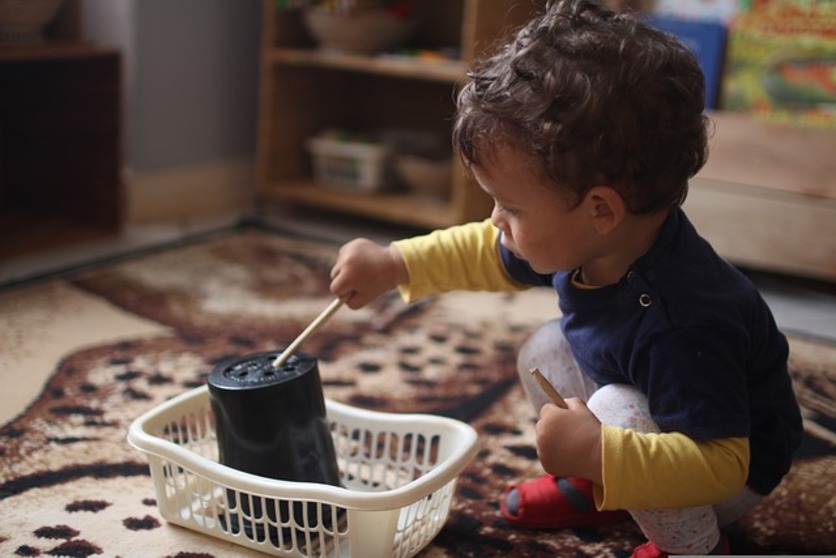 A imagem mostra uma criança brincando no chão com 3 objetos diferentes para ilustrar o fácil acesso a brinquedos no quarto montessoriano