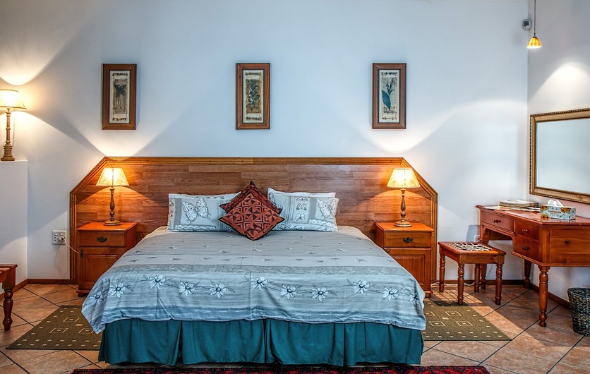 A imagem mostra um quarto com uma cama grande, com cabeceira de madeira, mesas laterais de madeira e uma penteadeira também de madeira para ilustrar o quarto do signo de câncer