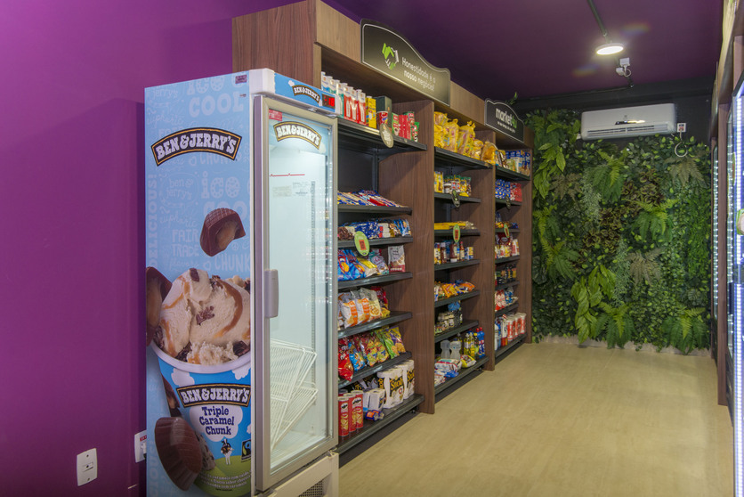 A imagem mostra um ambiente de minimercado, com várias prateleiras cheias de produtos de alimentação e higiene, ao lado de uma geladeira de sorvetes para ilustrar o Luggo Market do Luggo Parque Industrial