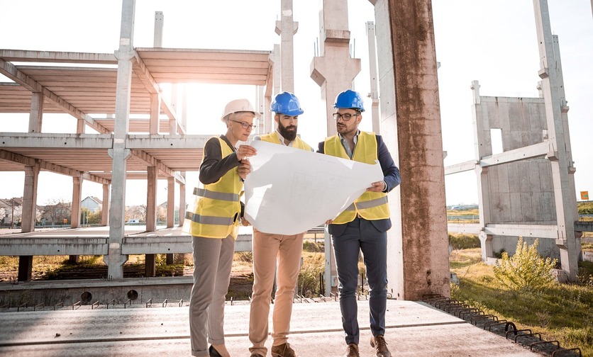 A imagem mostra um grupo de três pessoas em uma obra, com equipamentos de proteção e olhando para um grande papel de planejamento para ilustrar a Luggo como uma empresa verde