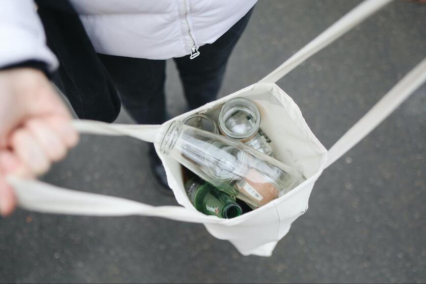 pessoa segurando uma sacola de pano com frascos de vidro para ilustrar reciclagem no consumo consciente