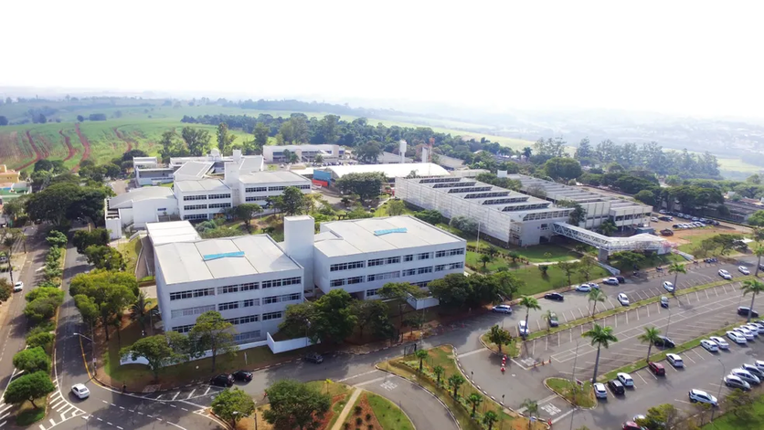 Foto aérea do campus da PUC-Campinas, durante o dia. Ao redor dos prédios, é possível ver uma região arborizada.