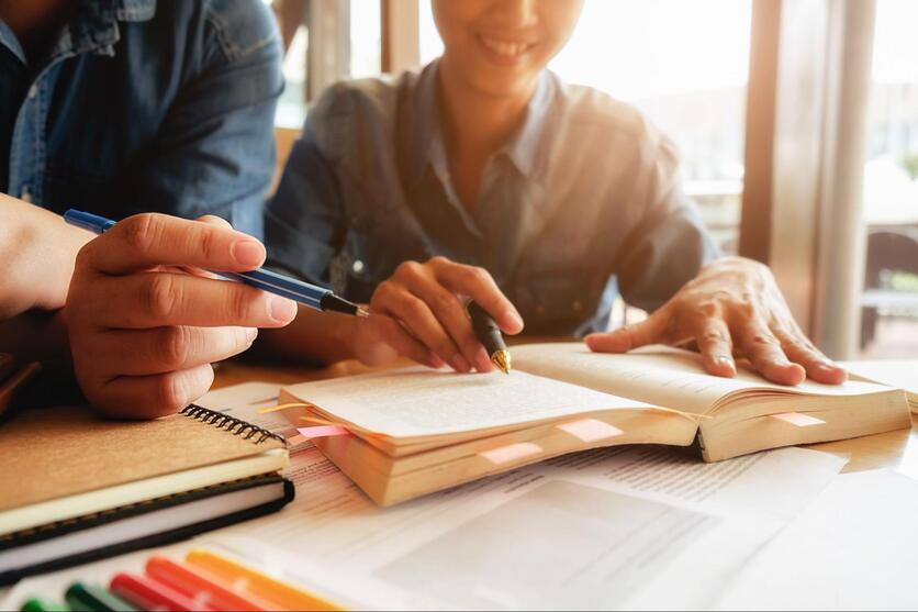 Duas pessoas estudando, com foco nos livros e cadernos em cima de uma mesa.