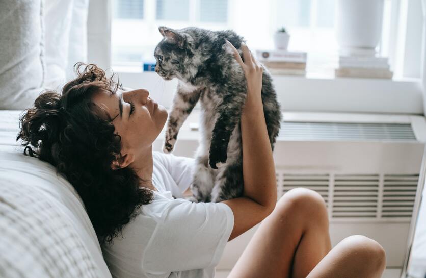 mulher apoiada em spfá na sala levantando um gato próximo ao rosto