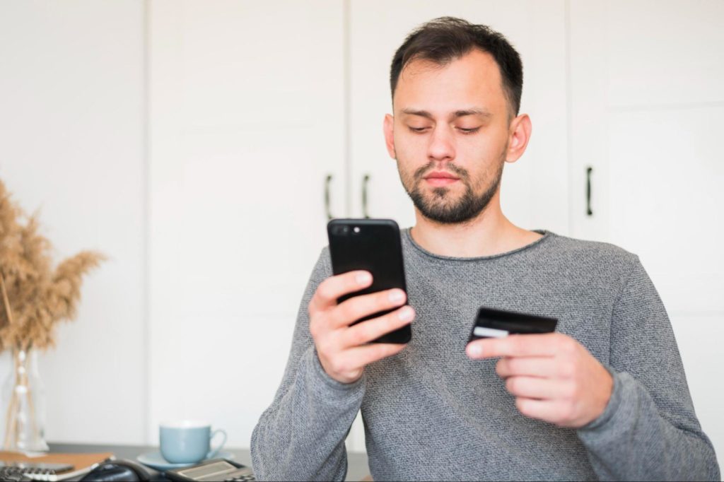 Inquilino checando o celular com um cartão na outra mão, pagando o aluguel pelo aparelho.