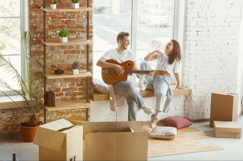 Casal hétero feliz rodeado de caixas descansando durante a mudança, o homem tocando violão.