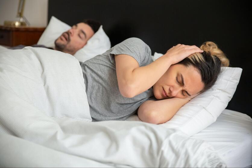 Casal tentando dormir, cobrindo os ouvidos com as mãos incomodado com o barulho.