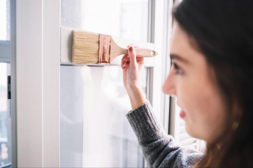 Mulher feliz com um pincel na mão, pintando uma janela.