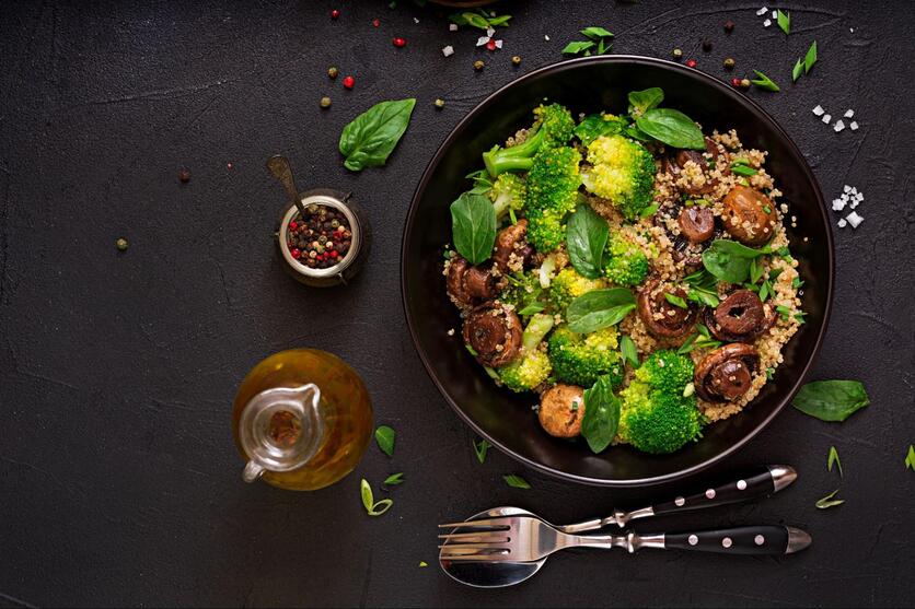 Visão de cima de prato de salada vegana sob uma mesa preta, decorado com condimentos e talheres em volta.