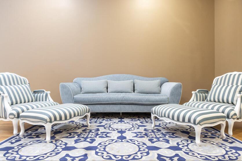 Ambiente decorado com móveis retrô: um sofá azul claro, duas poltronas listradas de azul e branco e um tapete estampado nas mesmas cores.
