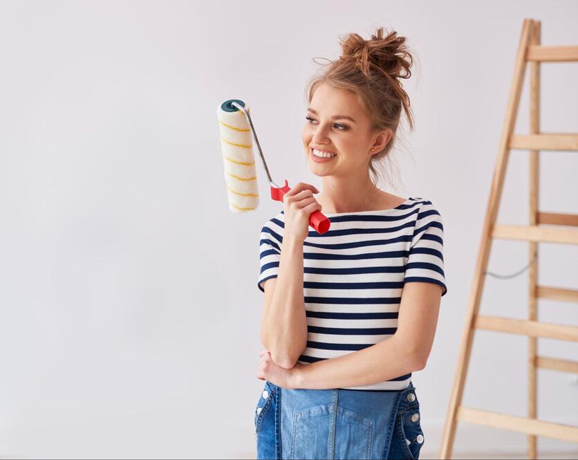 Mulher jovem segurando um rolo de pintura, sorrindo.