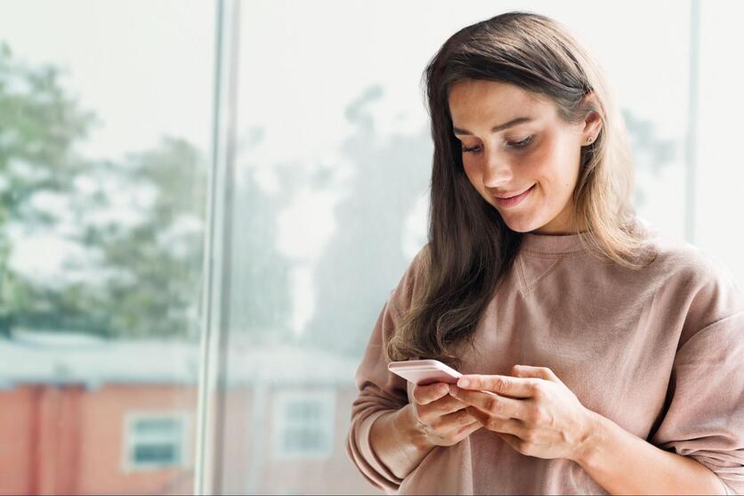 Mulher, com roupas casuais, digitando no celular durante um atendimento personalizado de uma administradora de condomínios.