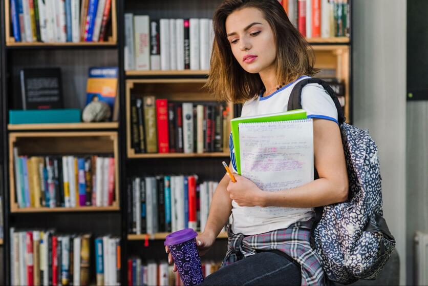 Mulher jovem, segurando nos braços materiais para a faculdade como livros, cadernos e lápis.