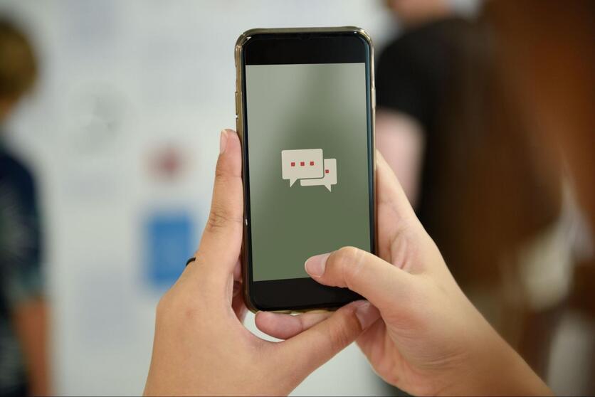 Duas mãos segurando um smartphone. Na tela, há um ícone de balões de conversa, simbolizando o atendimento online.