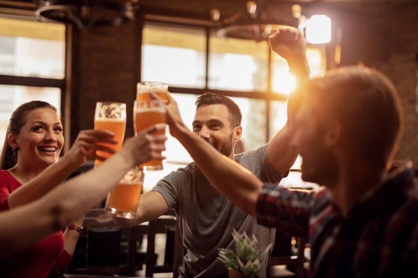 Jovens brindando cerveja, sorrindo, em um bar.
