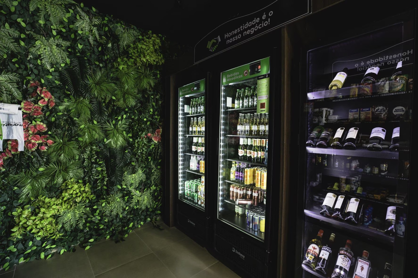 Espaço de bebidas da loja de conveniência Luggo, com decoração verde e uma placa com os dizeres “Honestidade é o nosso negócio!”