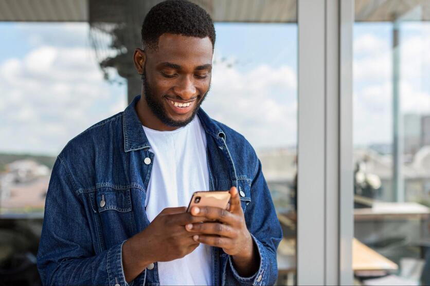 Homem negro sorrindo enquanto segura um smartphone, representando a facilidade do aluguel online.