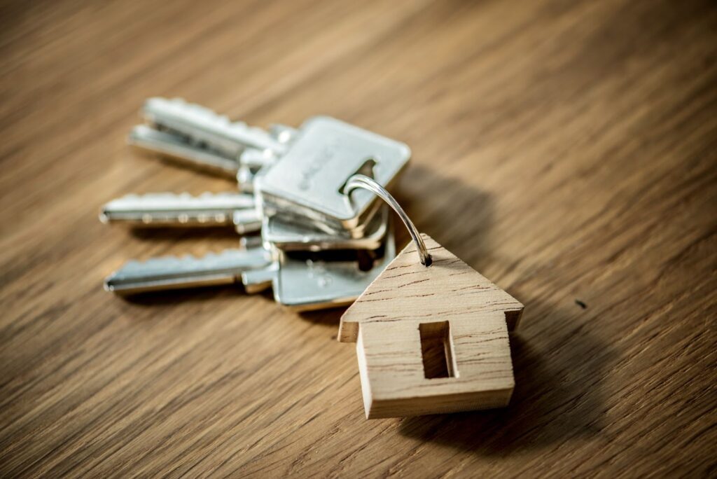 Chaves de apartamento, em cima de uma mesa de madeira, com um chaveiro de uma casa em miniatura.