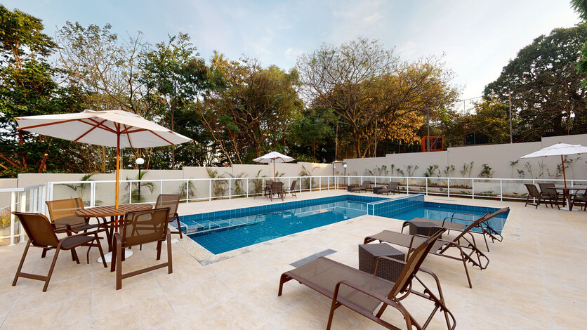 Piscina do Luggo Cenarium, cercada por cadeiras e mesas. Ao fundo, é possível ver a vegetação natural preservada ao redor do condomínio.