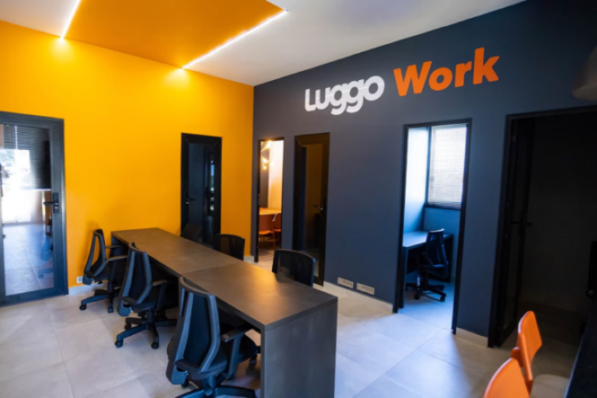 Espaço coworking moderno, com decoração em preto e laranja, incluindo pequenas salas de conferência e uma sala ampla com mesa compartilhada.