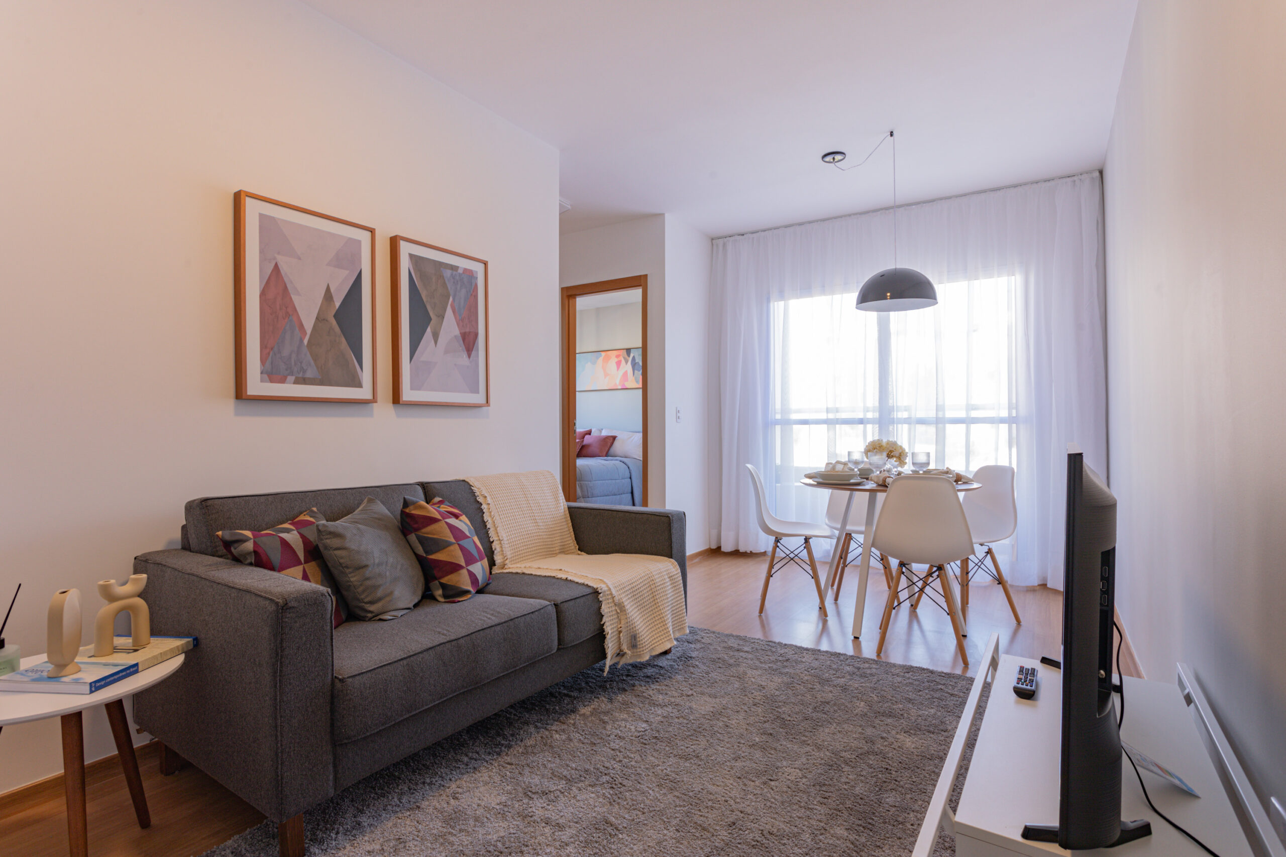 Sala de estar de apartamento do Luggo Buritis, decorada com sofá, tapete, quadros e rack.
