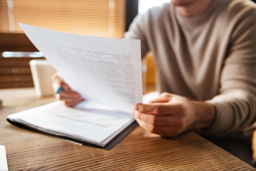 A imagem mostra um homem segurando um contrato na mão. O fundo está desfocado, evidenciando o papel.