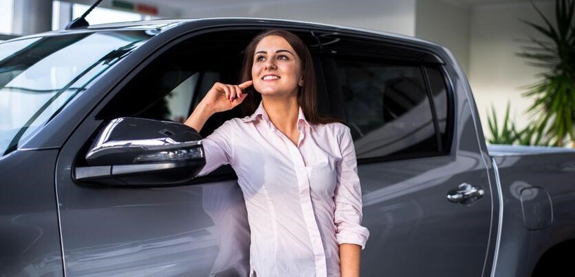 Mulher em uma garagem em condomínio, ela está com o corpo voltado para trás, acionando o alarme de um carro que está estacionado.