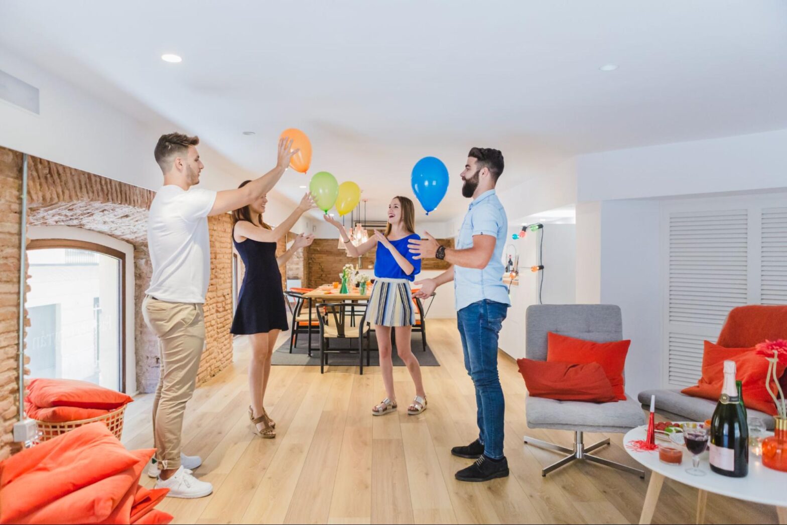 Dois homens e duas mulheres celebrando e segurando balões coloridos em um salão de festas do condomínio com decoração alegre.