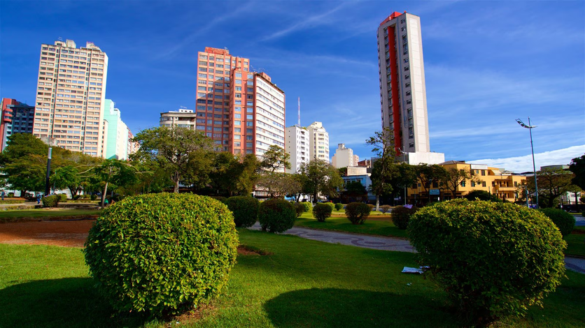 Vista do Parque Municipal com arbustos podados e gramado, cercado por edifícios altos sob um céu azul, refletindo a urbanidade de Belo Horizonte.