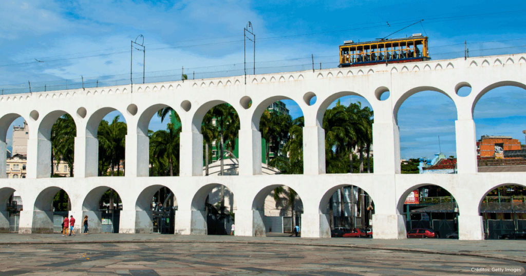 Foto noturna ou diurna dos Arcos da Lapa, no Rio de Janeiro, uma imponente estrutura branca de estilo colonial (aqueduto) em destaque, simbolizando a riqueza histórica e a vida cultural do Centro. A imagem reforça a localização privilegiada do condomínio Luggo Mauá, situado nas proximidades.
